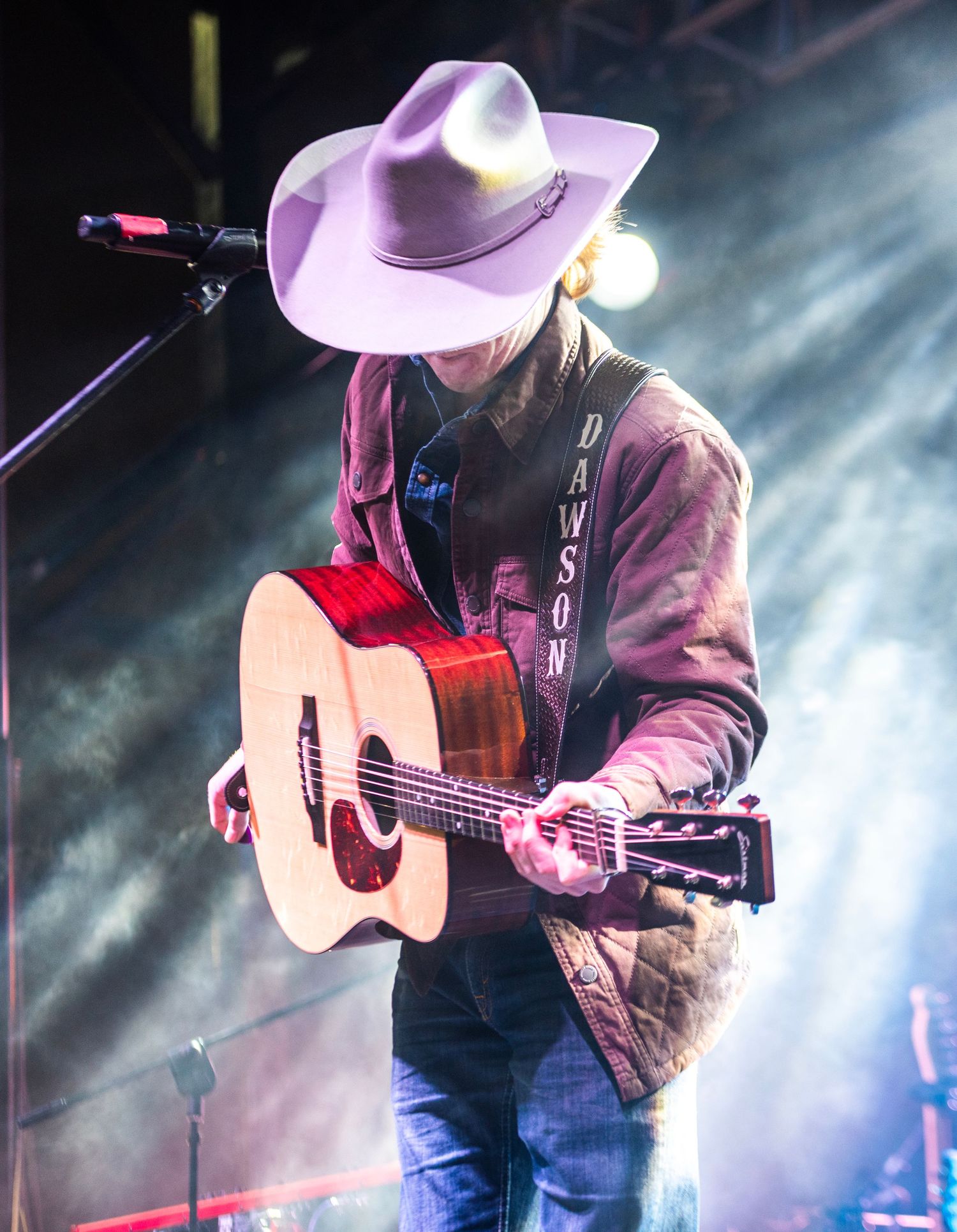 Country artist Dawson performing on stage with acoustic guitar under dramatic stage lighting.