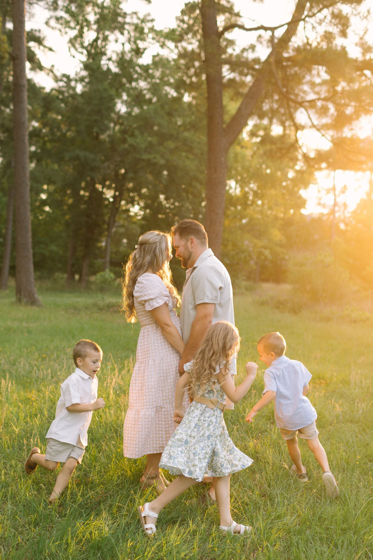 Family of five enjoying a golden sunset in a green park, parents embracing while three children play around them.