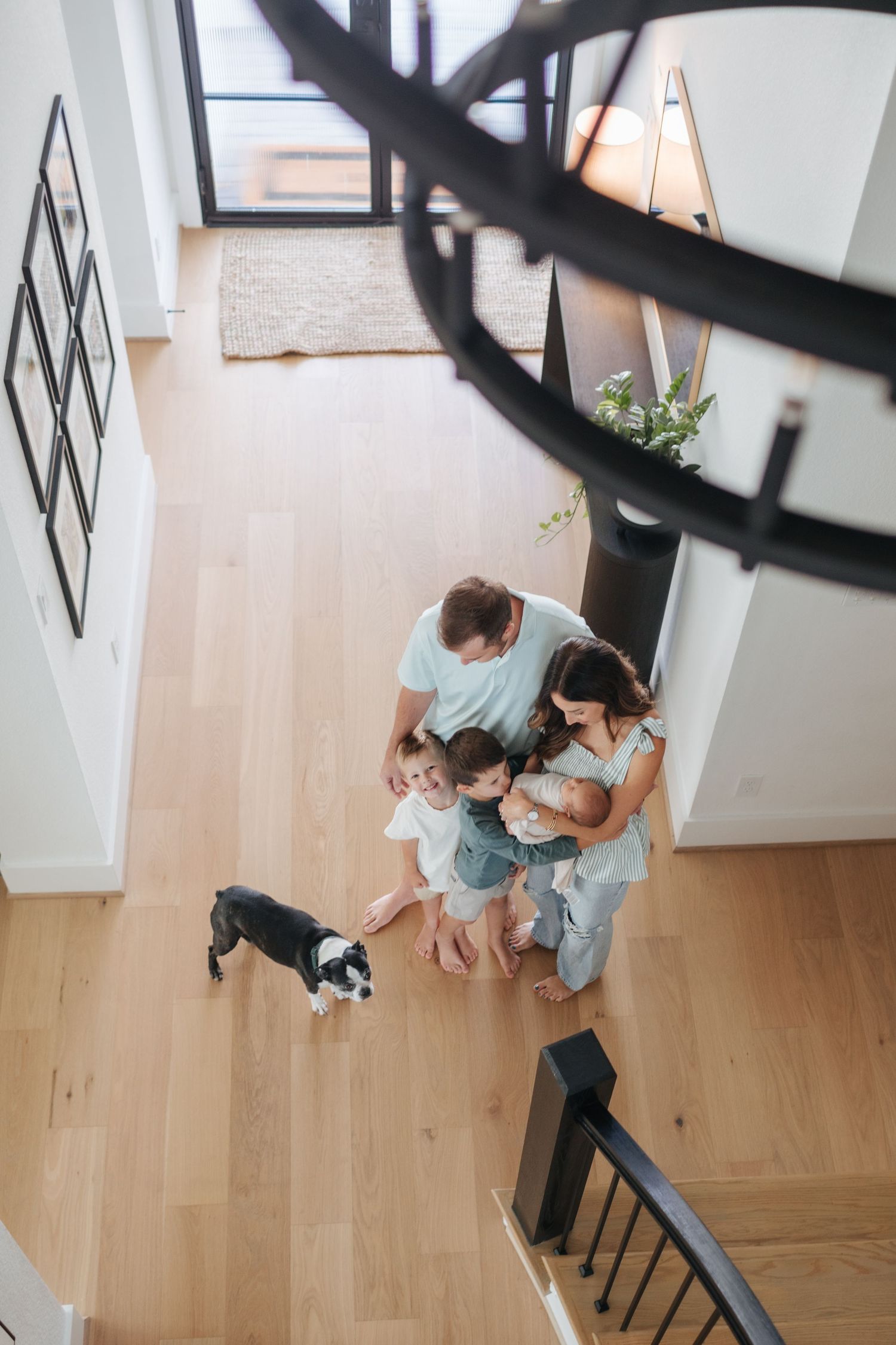 Aerial view of family with newborn and dog standing on hardwood floor of modern home.