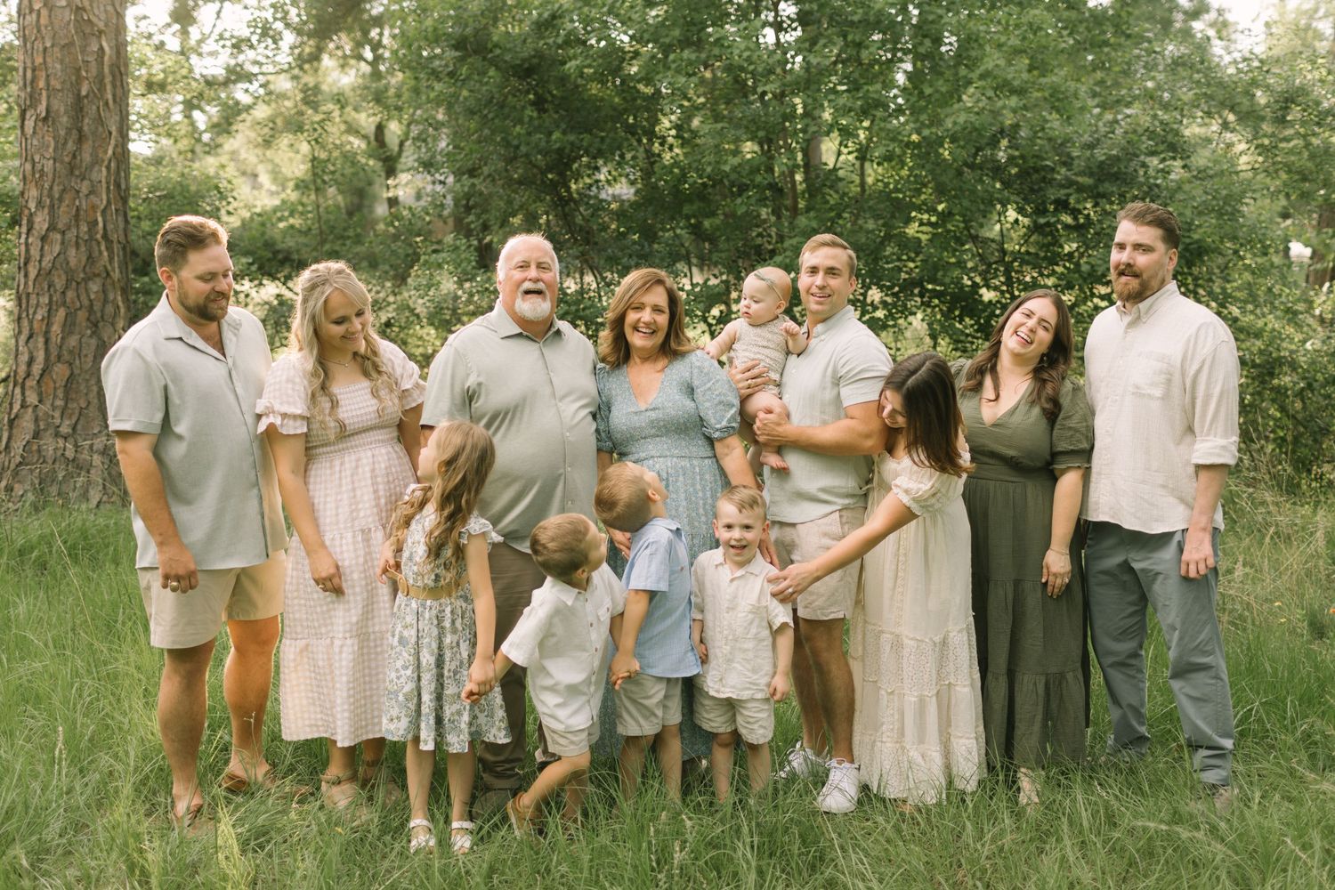 Large multigenerational family smiling together outdoors in a lush green park setting for a professional portrait.