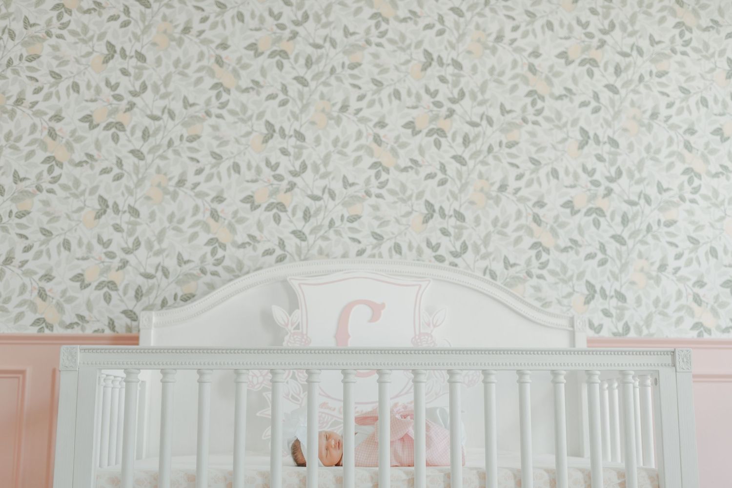 White wooden baby crib against a soft floral wallpaper in a pastel nursery room.