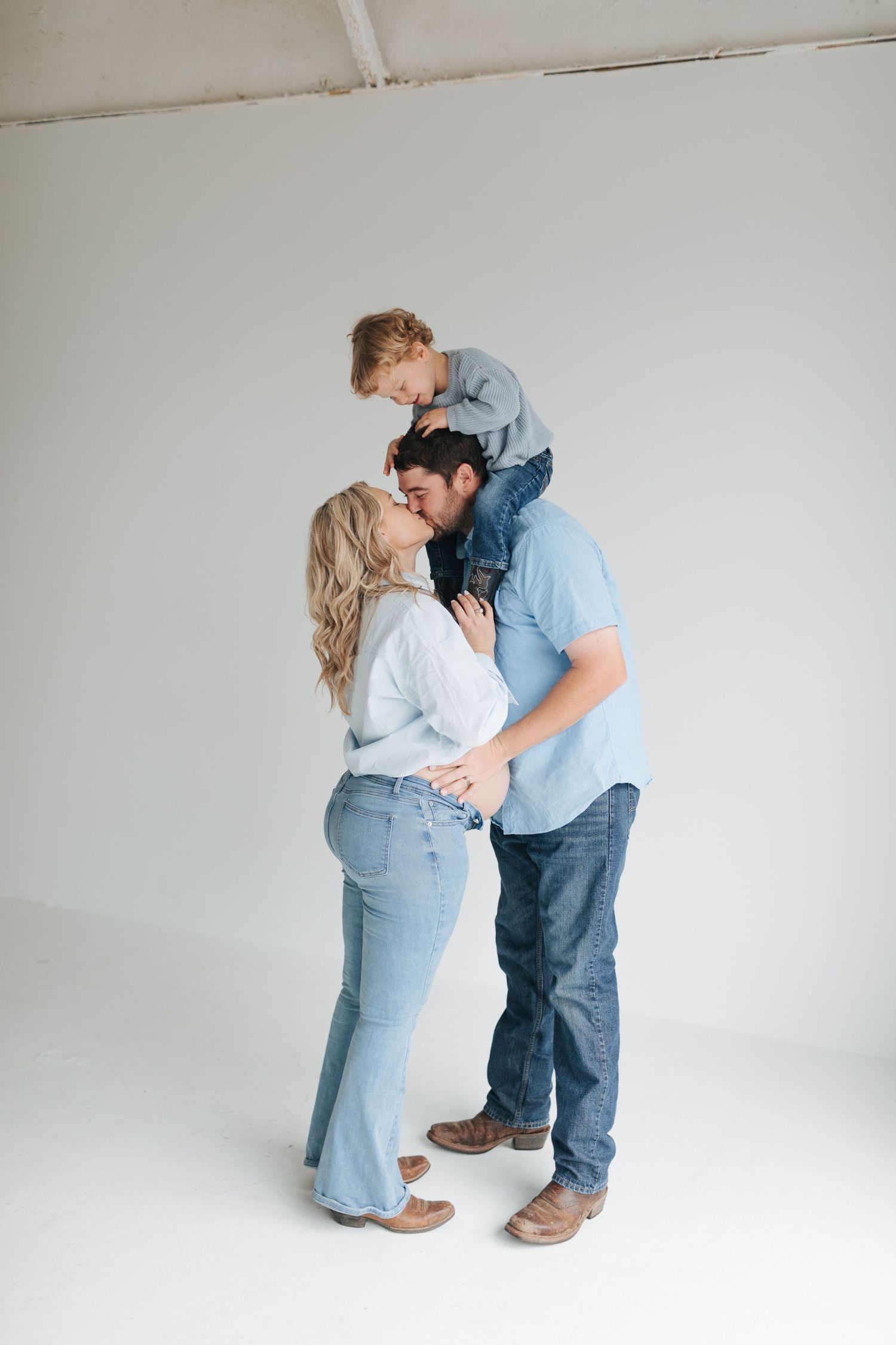 Happy family maternity photo with pregnant mother, father, and young son in coordinating blue denim outfits.
