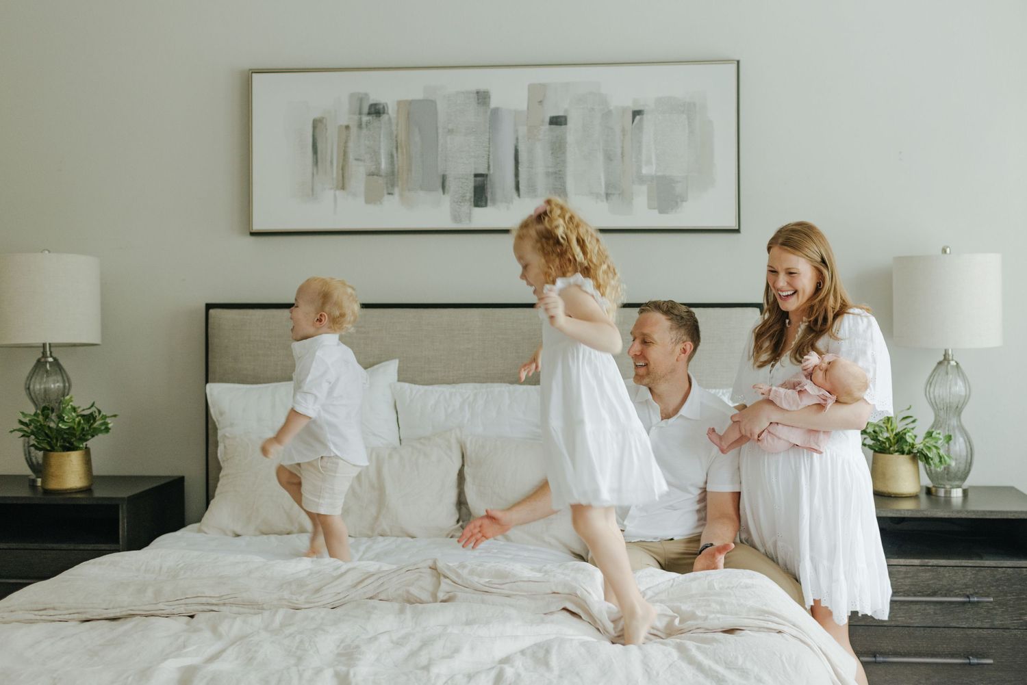 Joyful family with young children and newborn bonding together on a cozy white bed at home.