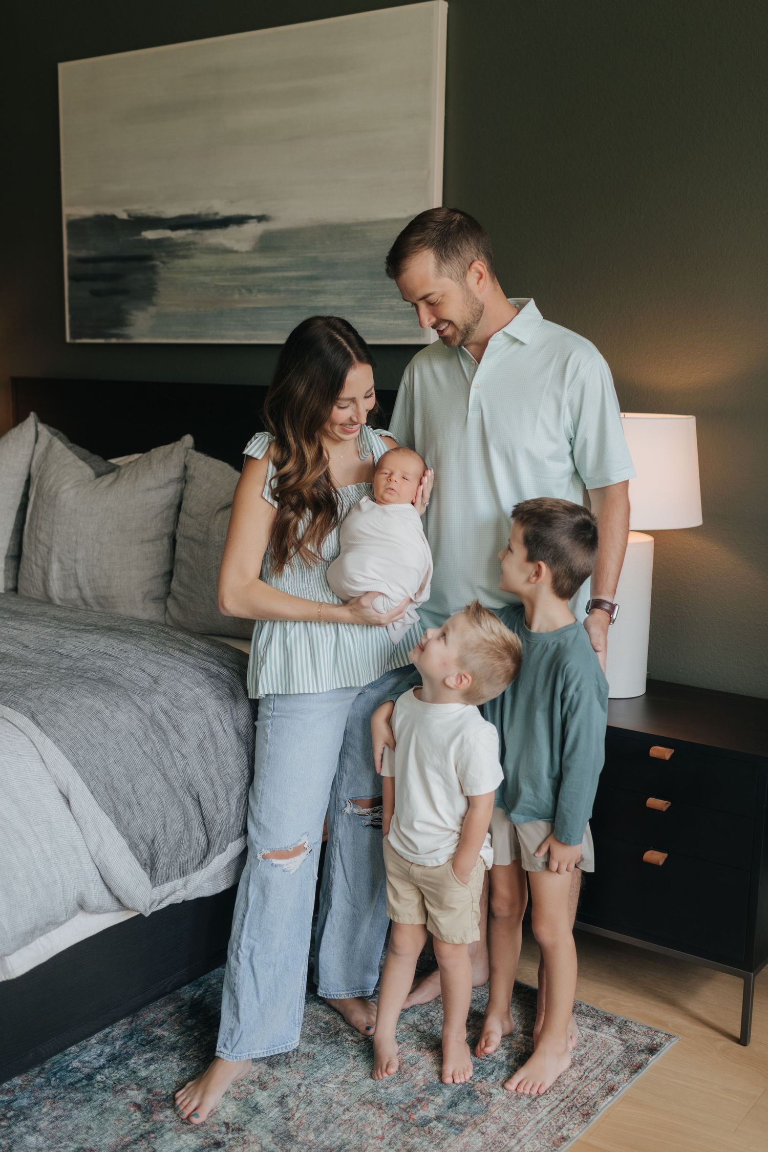Happy family of five with newborn baby gathered together in a stylish bedroom setting.