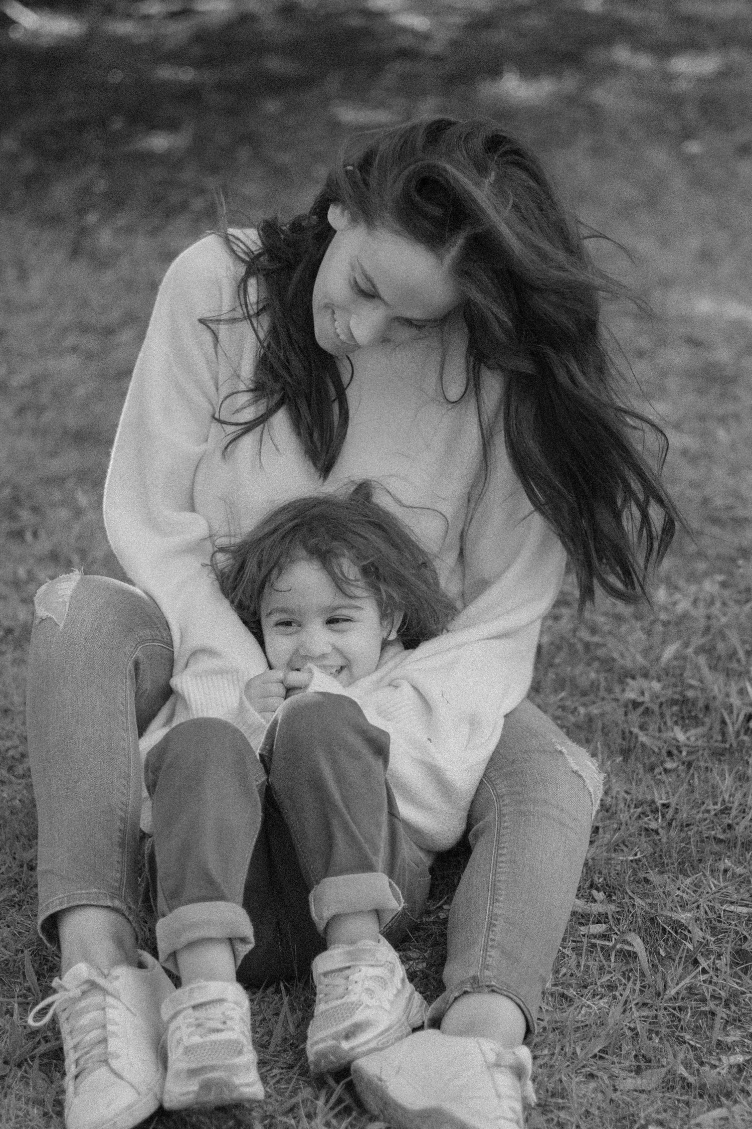 Black and white photo of mother sitting on grass smiling at laughing young child.