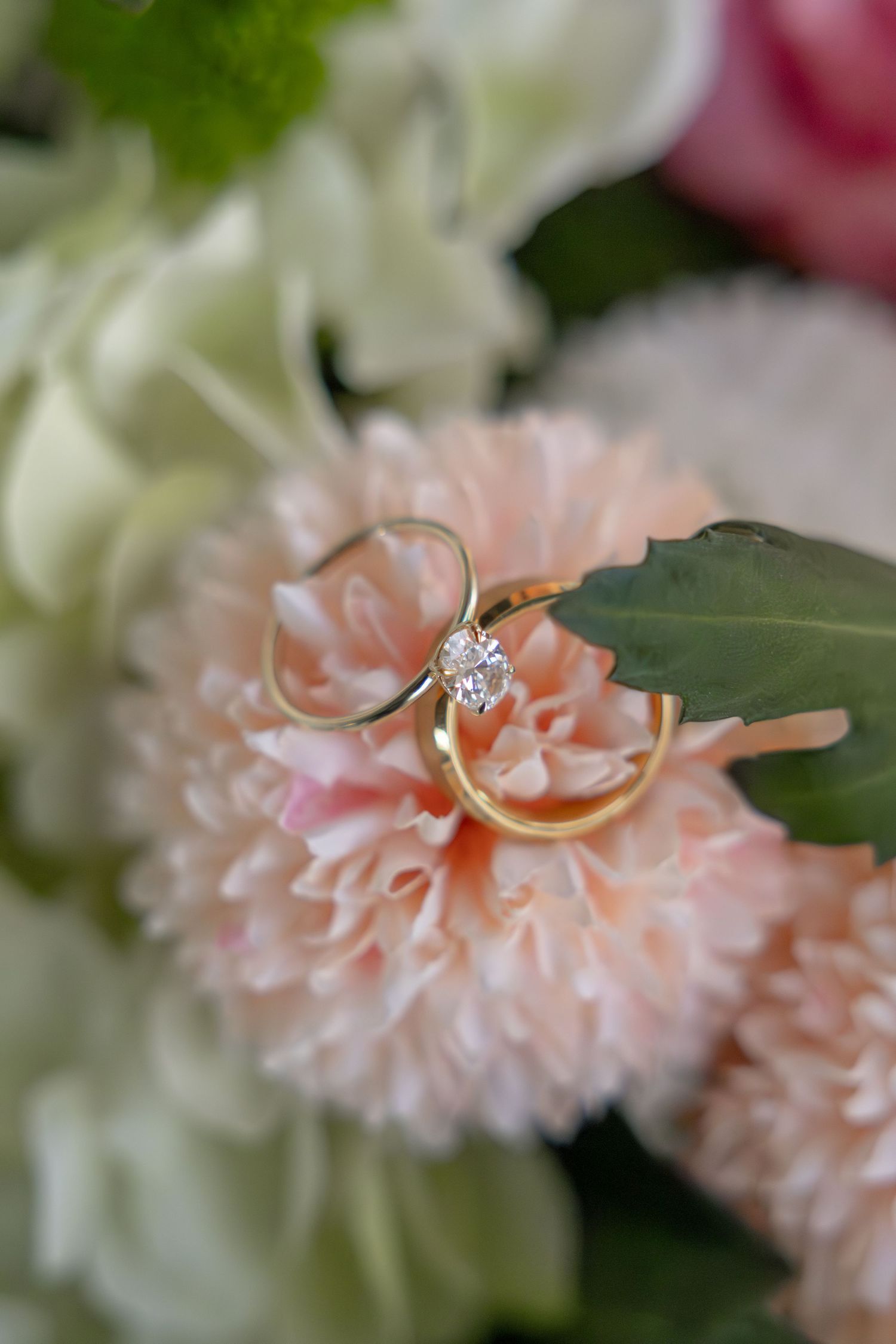 Two gold wedding rings resting on pink carnation flower in bridal bouquet.