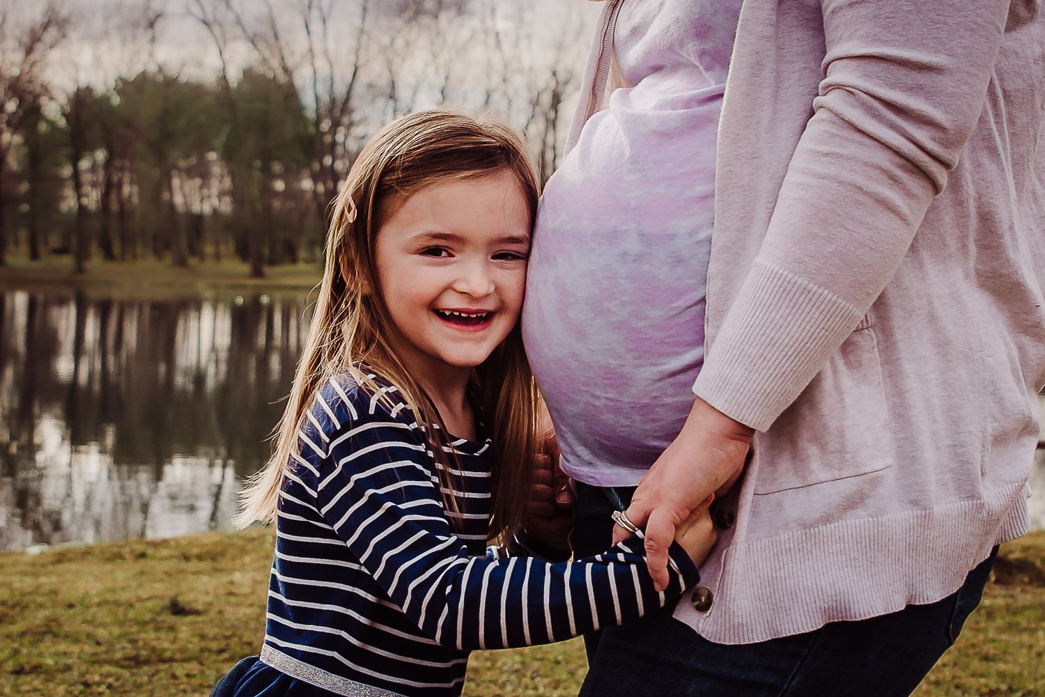 Family photographer based in Winchester, Virginia.  Little girl hugs close to mom's pregnant belly to hear baby