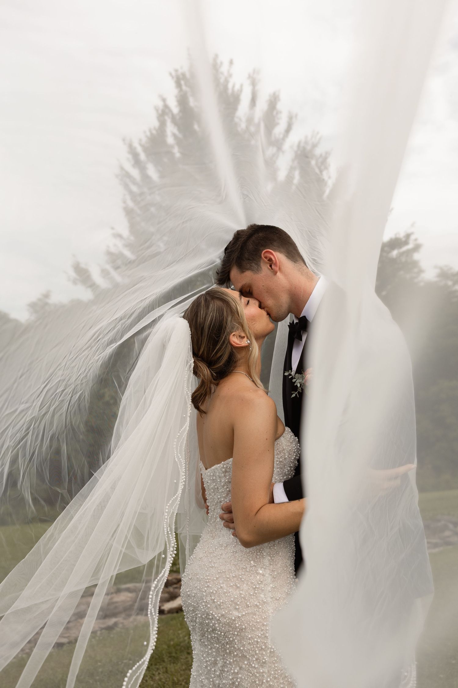 Bride and groom share romantic moment under flowing white veil outdoors on their wedding day.