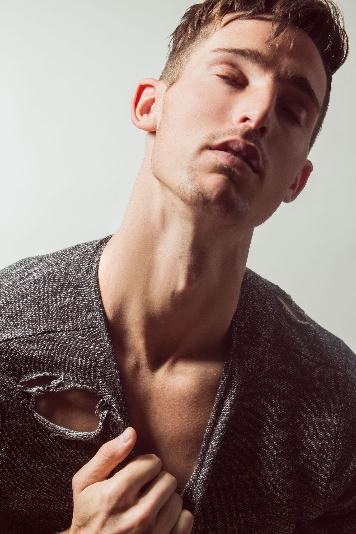 Young man in a distressed gray knit sweater posing confidently against a light background.