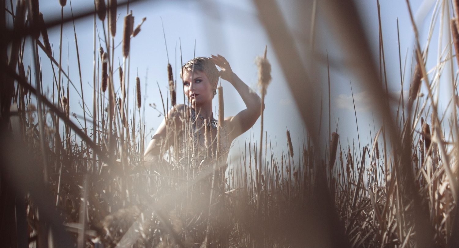 Person standing among tall cattails in sunlit field, shielding eyes from bright natural light.