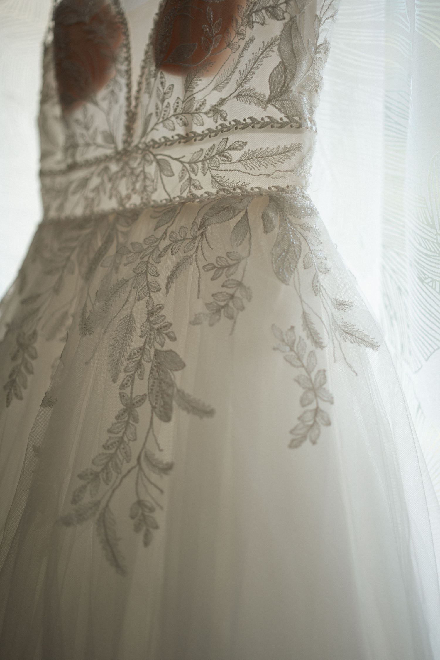 Close-up of an elegant wedding gown featuring intricate floral lace embroidery on soft ivory tulle fabric.