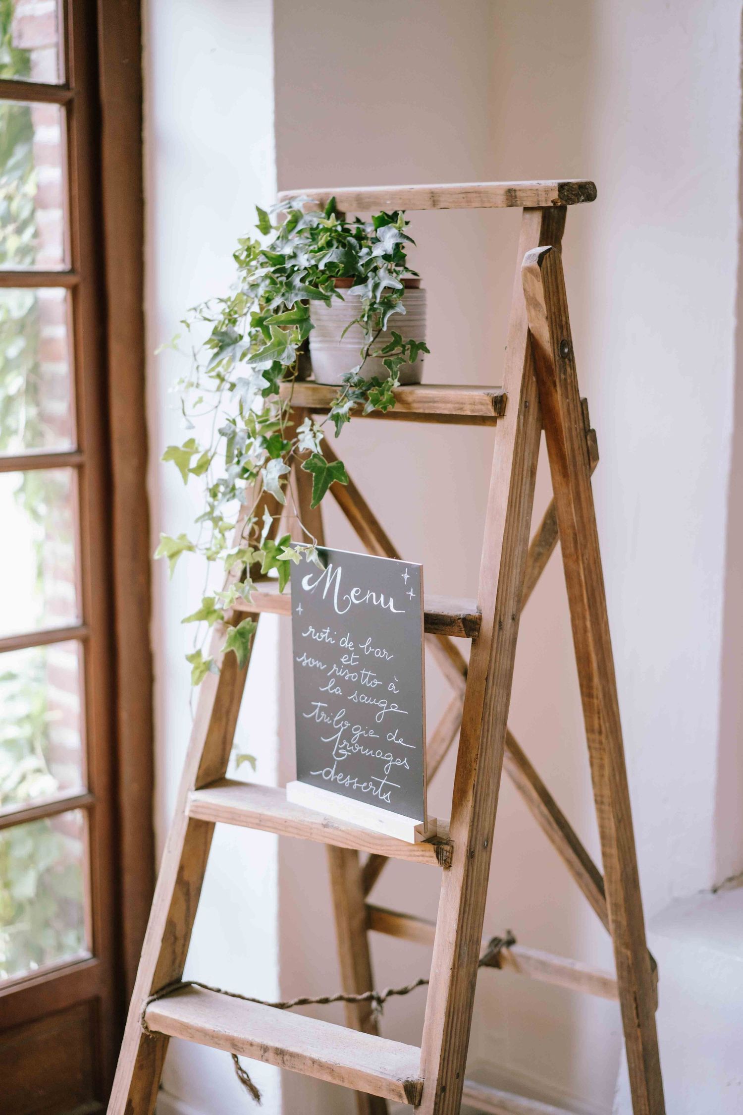 Décoration de mariage rustique avec échelle en bois, lierre et tableau noir avec menu écrit à la main.