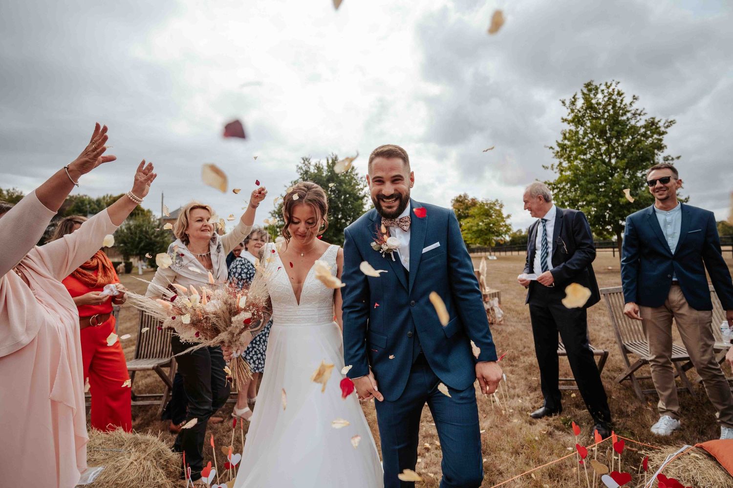 Les jeunes mariés, rayonnants de bonheur, traversent une pluie de confettis colorés lancés par les invités en fête.