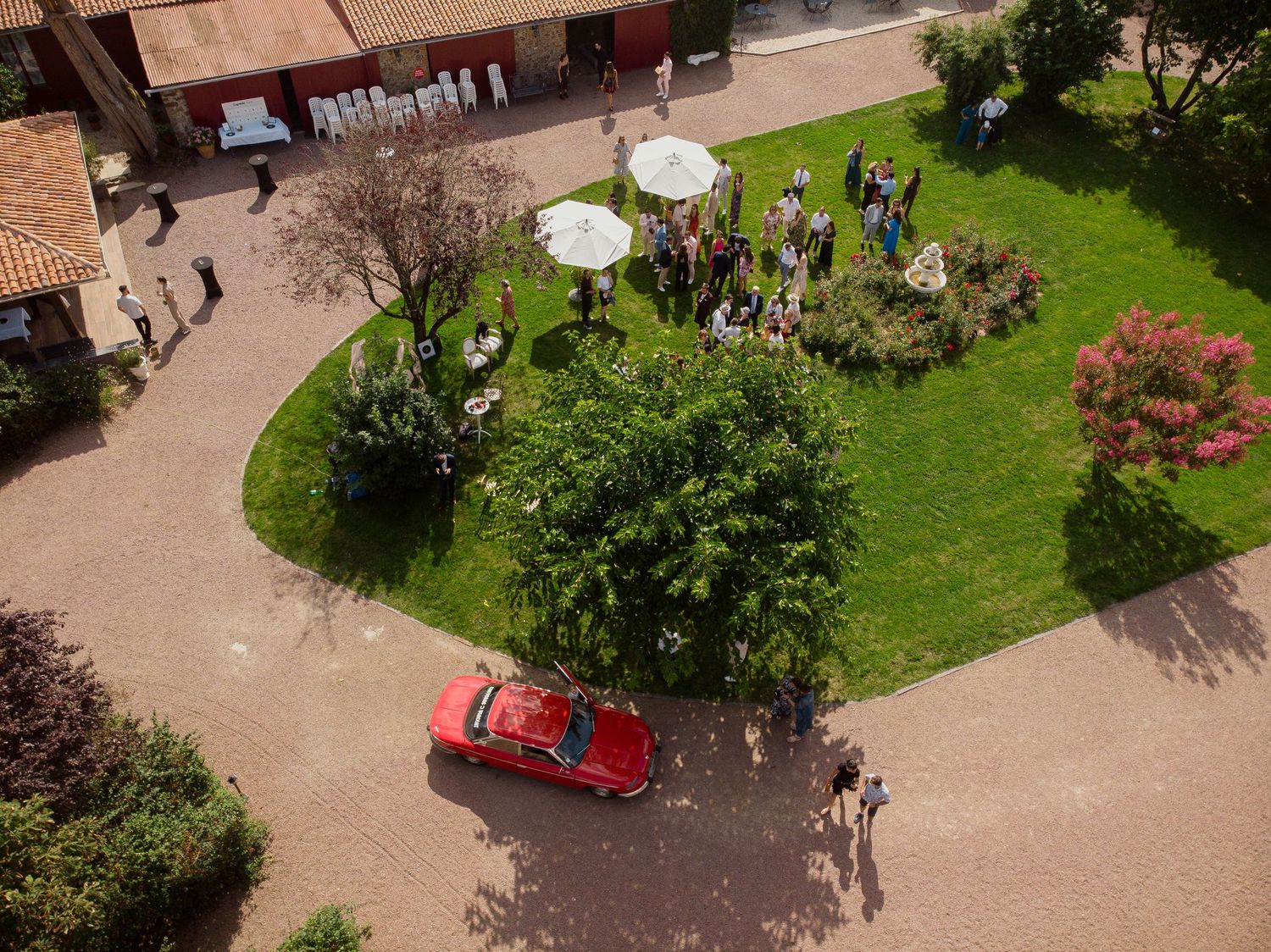 Photo de mariage au drone dans un domaine – Vue aérienne des invités rassemblés dans un jardin verdoyant, avec voiture rouge ancienne au pre