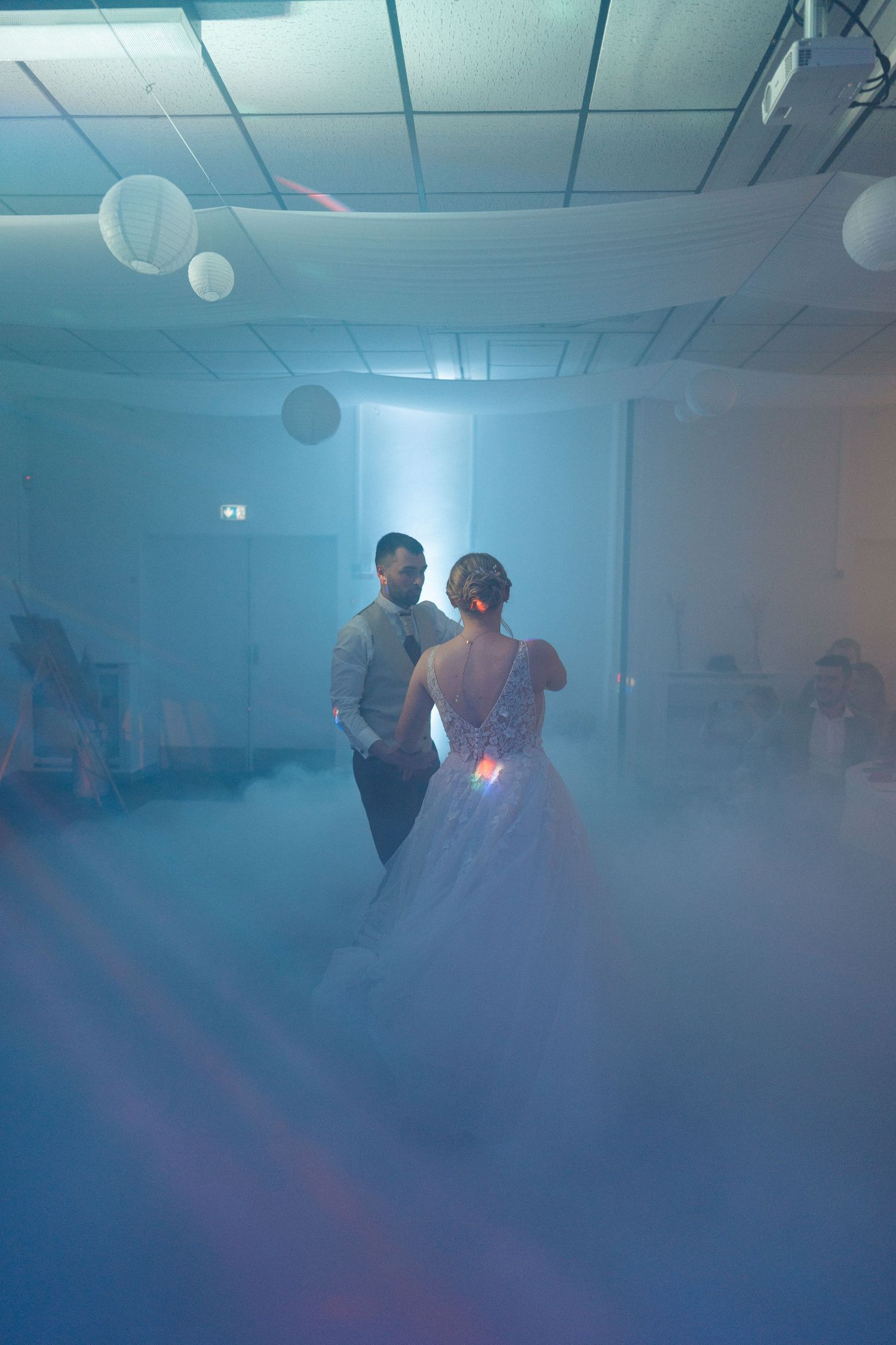Bride and groom share their first dance surrounded by fog machine smoke and soft blue lighting at their wedding reception.