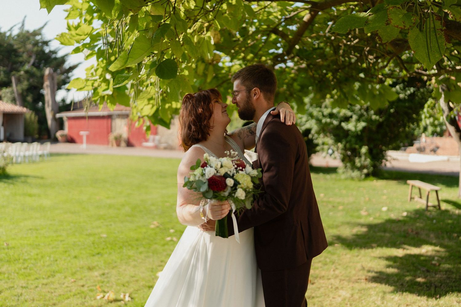Les mariés partagent un moment intime sous un feuillage vert lors d'un mariage en plein air.
