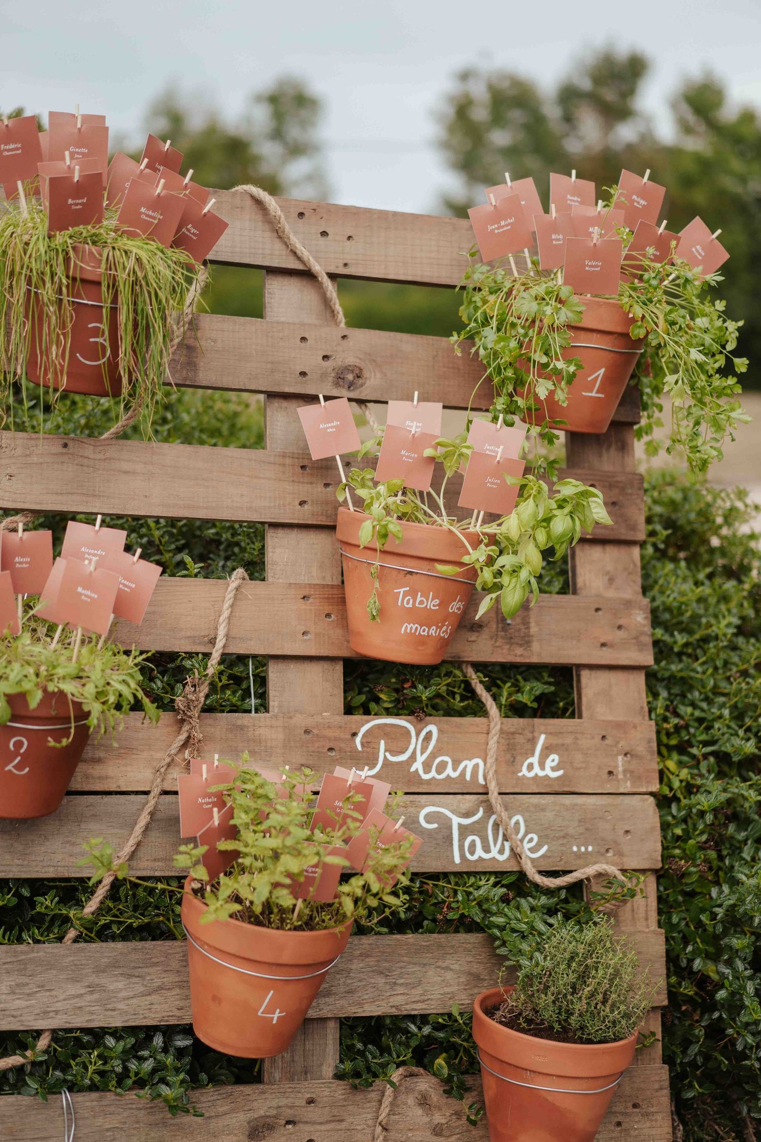 Plan de table rustique pour un mariage, réalisé avec des palettes en bois, des pots en terre cuite, des herbes aromatiques et des numéros