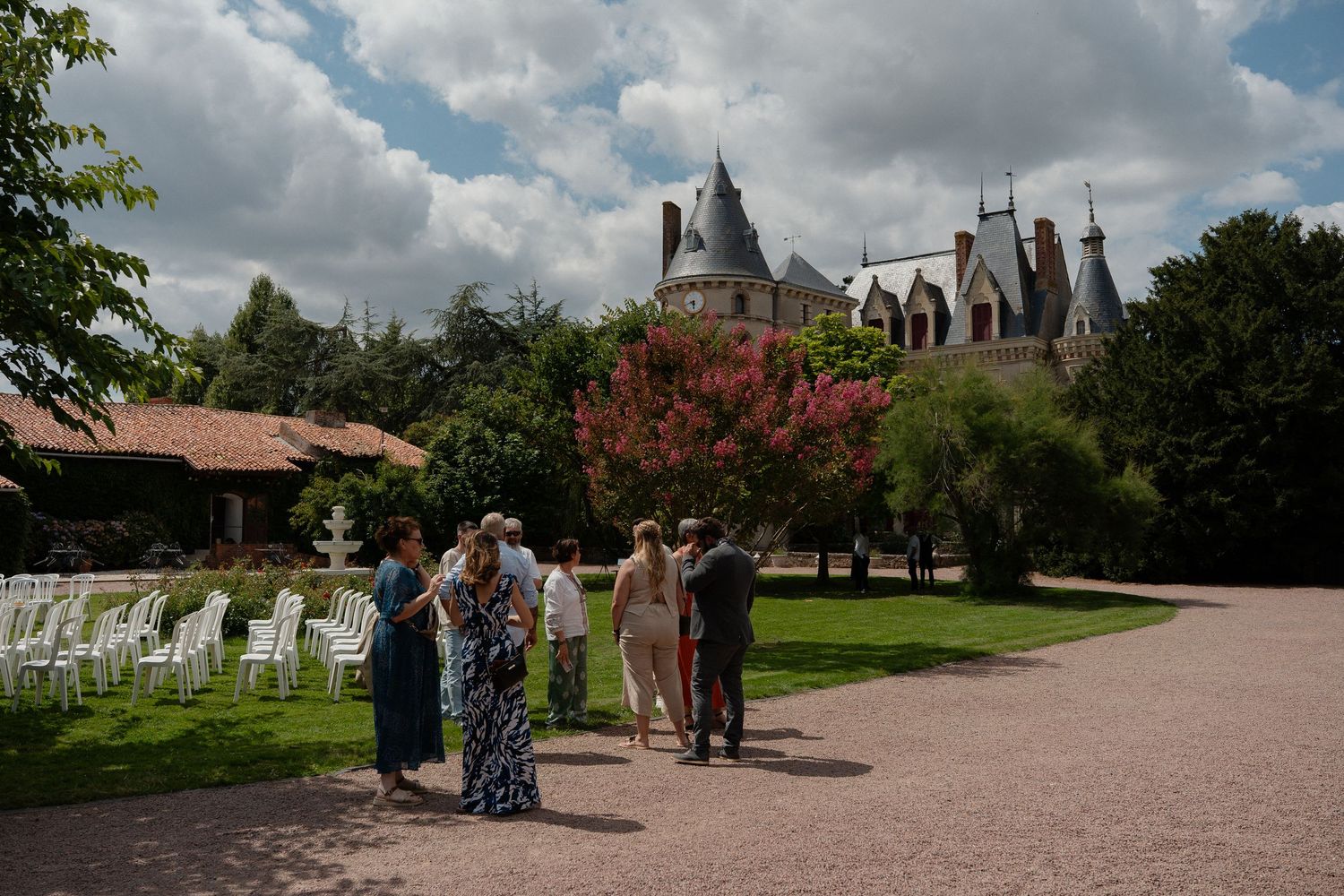 Les invités se rassemblent dans le jardin d'un château français, où des chaises blanches sont disposées pour une cérémonie de mariage .