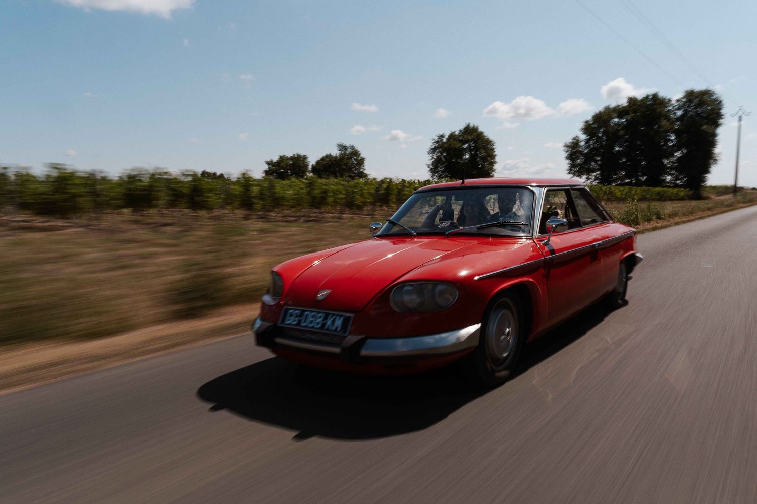 Voiture classique rouge vintage filant à toute allure sur une route de campagne entourée de vignes.