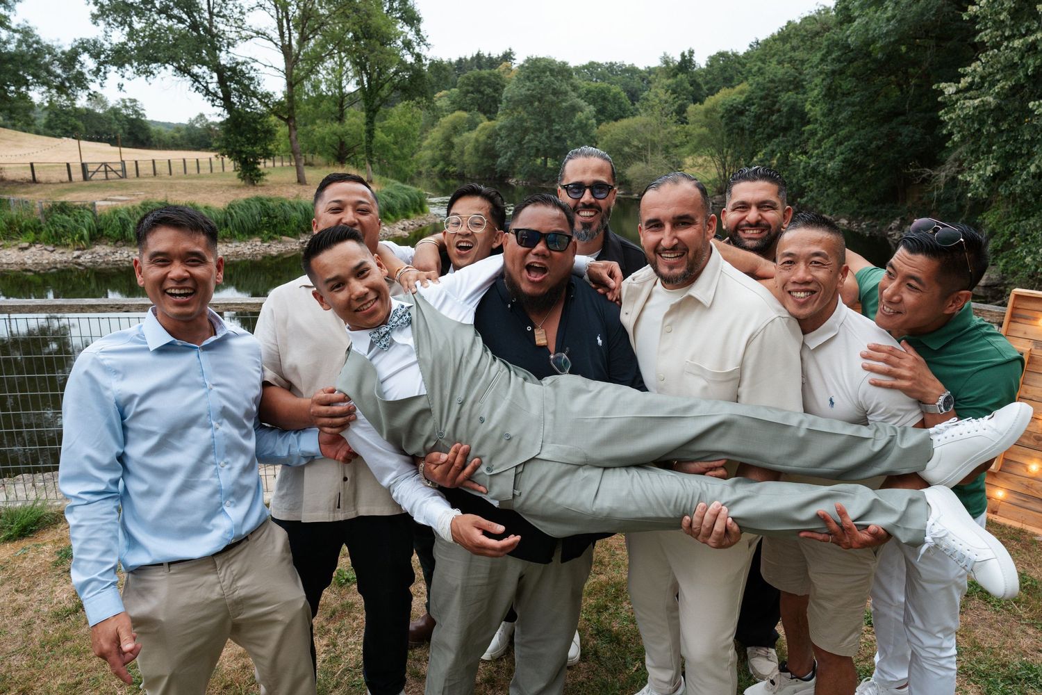 Group of men smiling outdoors, lifting one man horizontally, celebrating together near a garden fence.