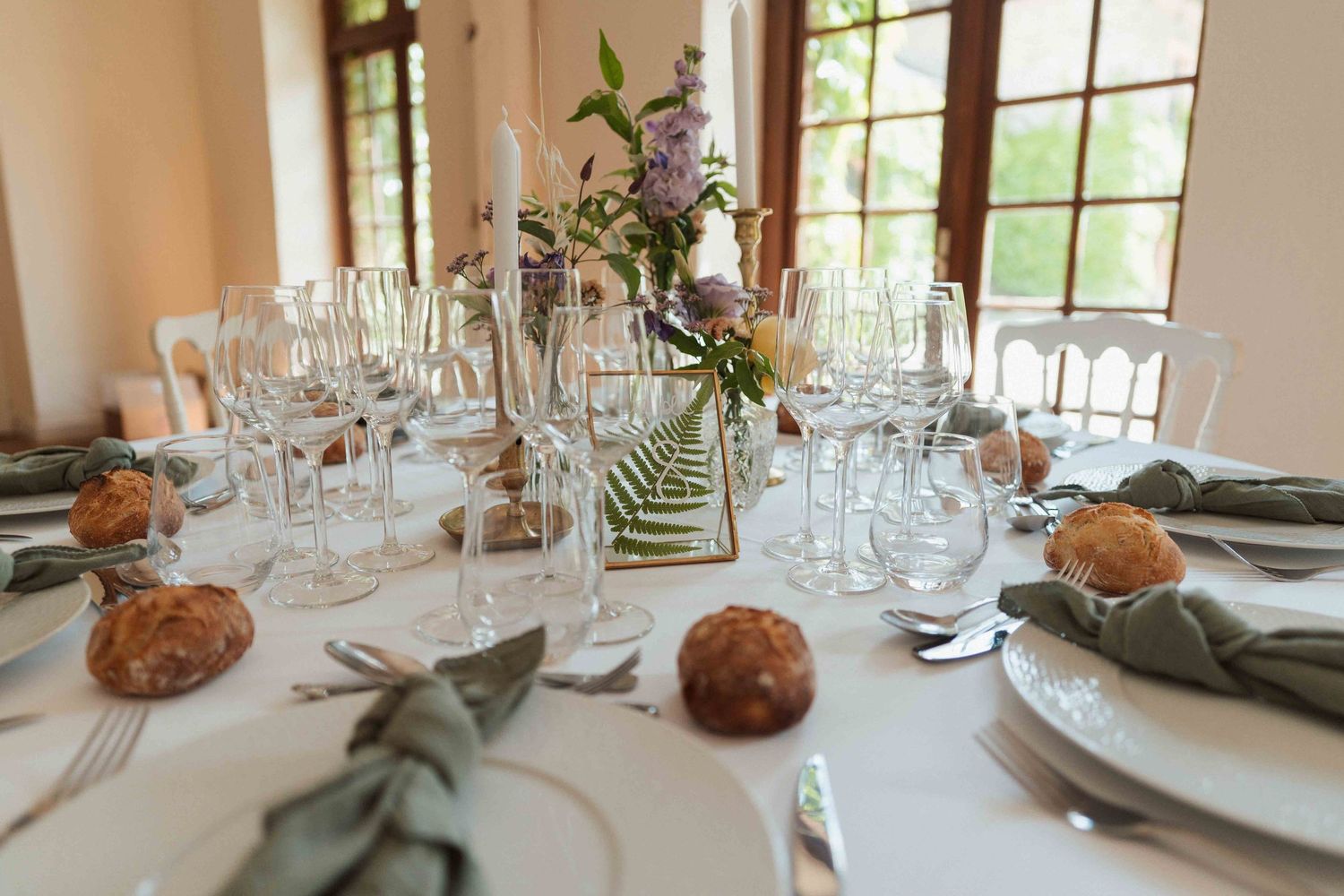 Élégante table de réception de mariage dressée avec de la verrerie, des serviettes couleur sauge et un centre de table floral.