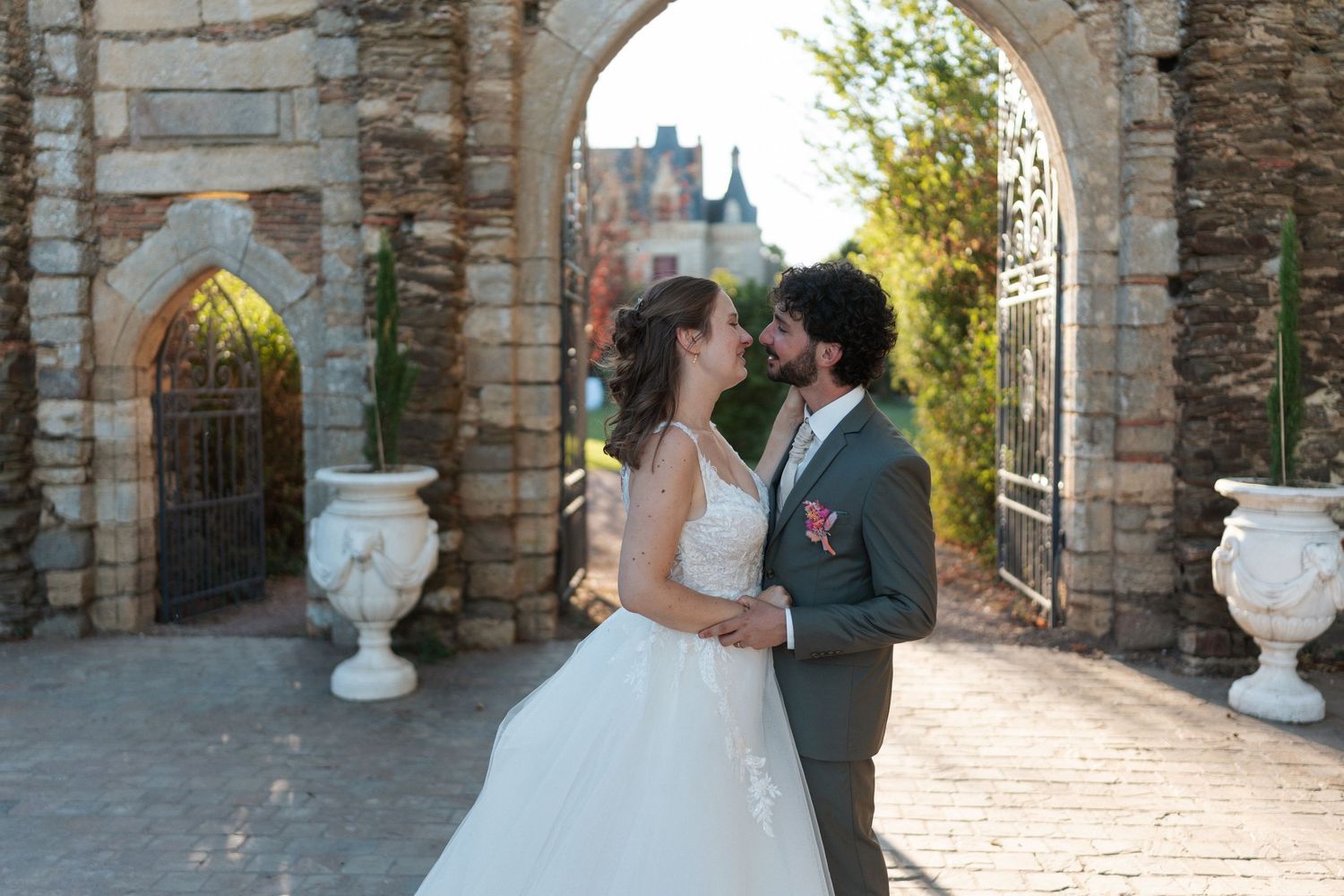 Bride and groom share a romantic moment under a stone arch at a castle wedding venue.