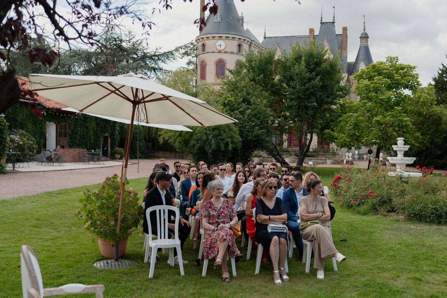 Invités assis dans le jardin du Château des Landes à Cléré-sur-Layon – Cérémonie laïque de mariage avec parasol et fontaine en arrière-plan.