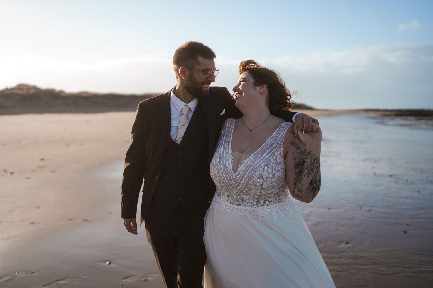 Les mariés, rayonnants de bonheur, se promènent main dans la main sur une plage ensoleillée le jour de leur mariage.