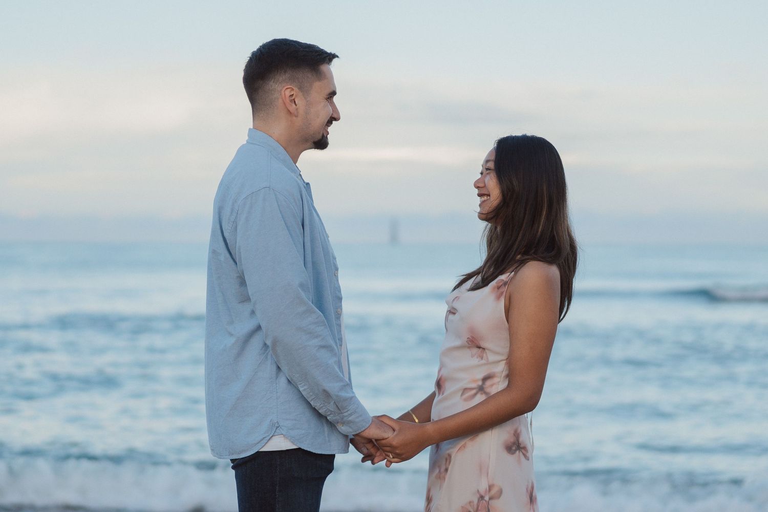 Séance engagement au bord de l’océan – Les futurs mariés échangent un regard complice face aux vagues.