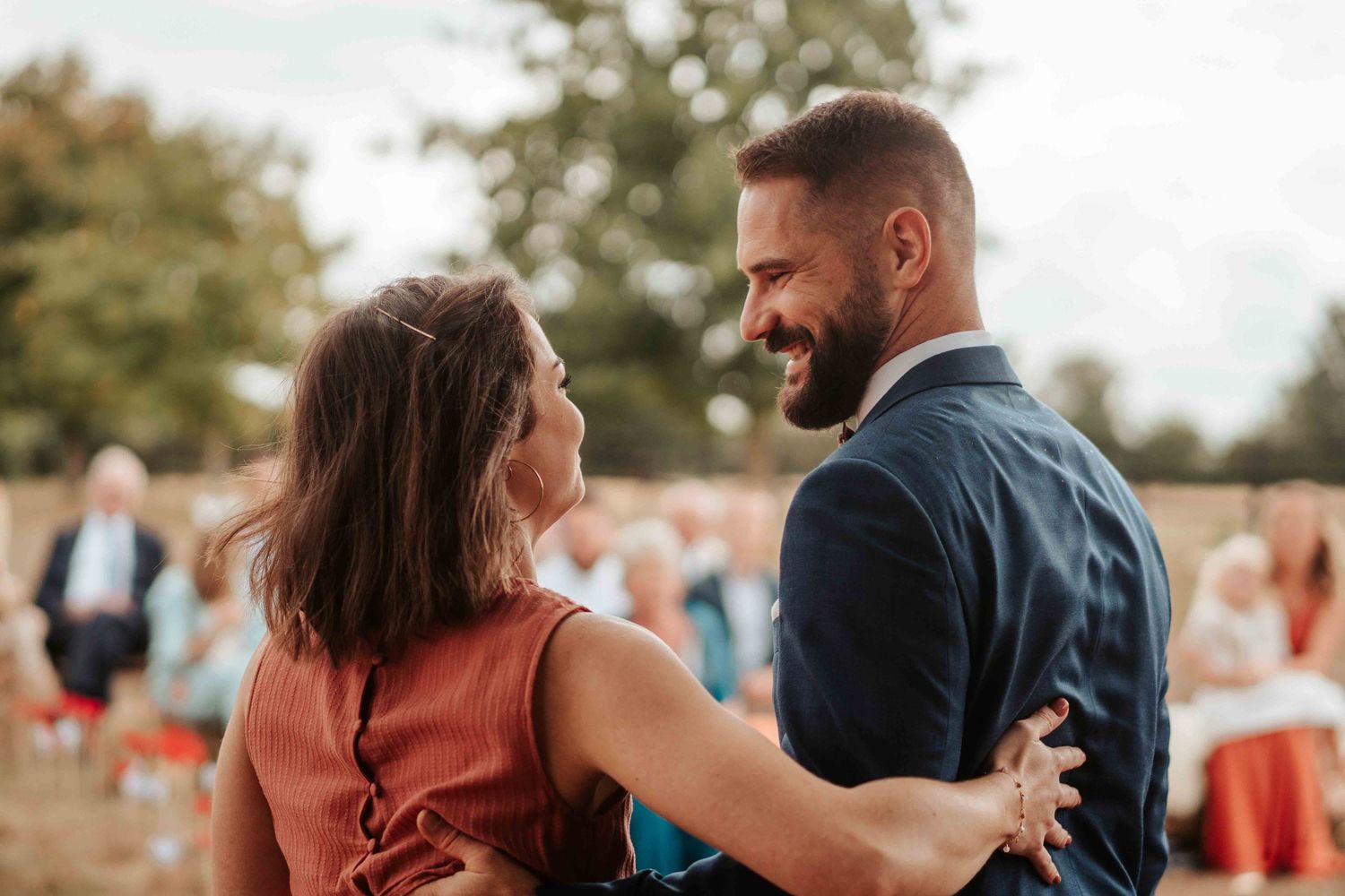 Un couple souriant danse en plein air lors d'une réception de mariage, avec les invités en arrière-plan.