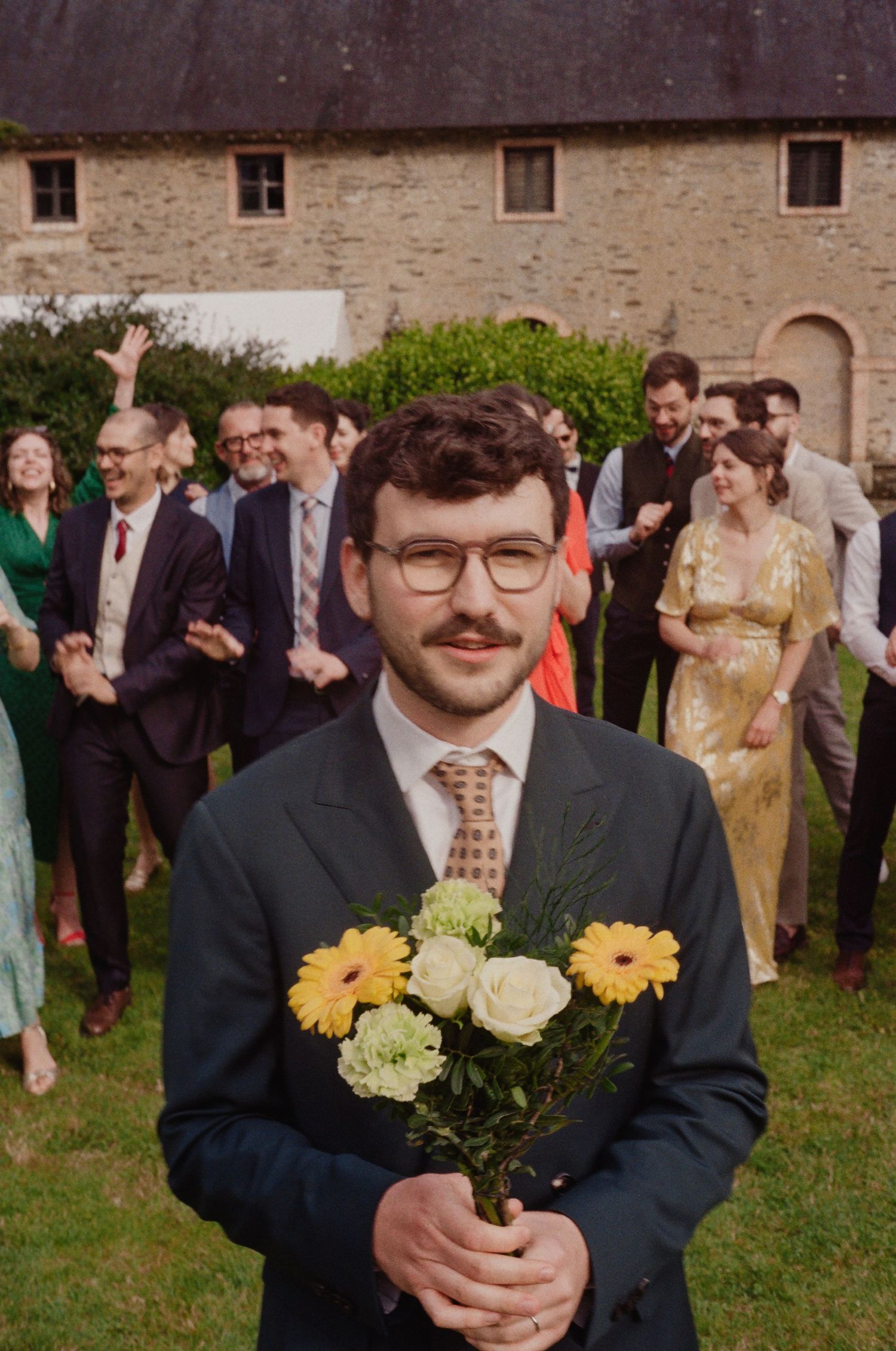 Mariage en argentique – Témoin tenant un bouquet de fleurs devant les invités – Scène spontanée et joyeuse.