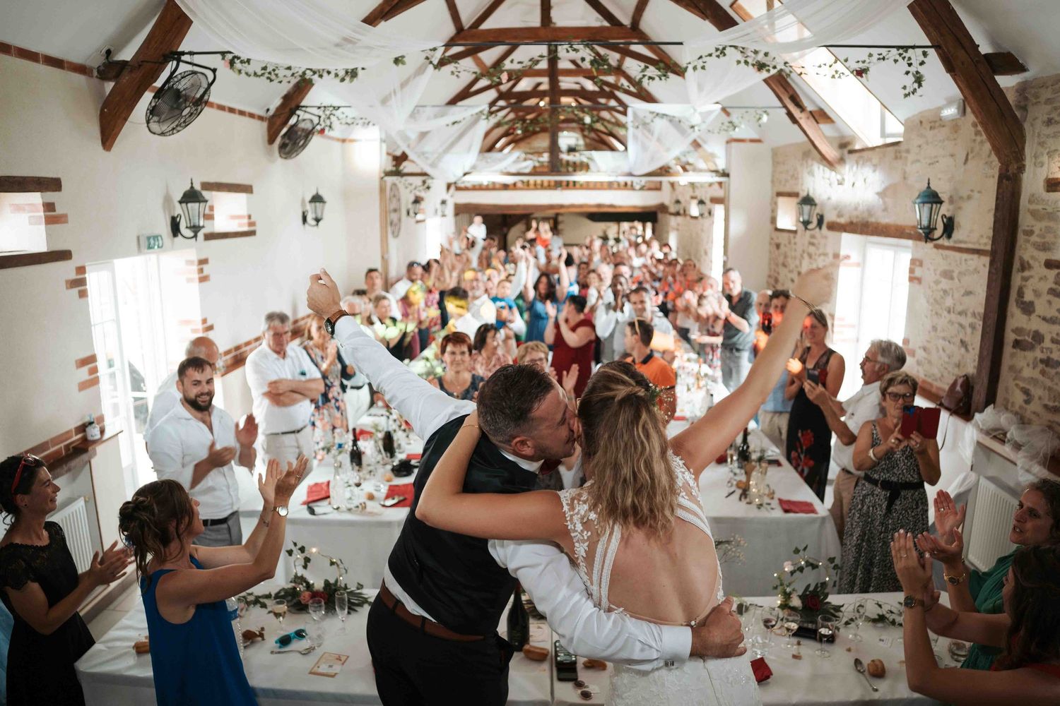 Les mariés échangent un baiser romantique sous les applaudissements des invités lors d'une réception dans une grange rustique