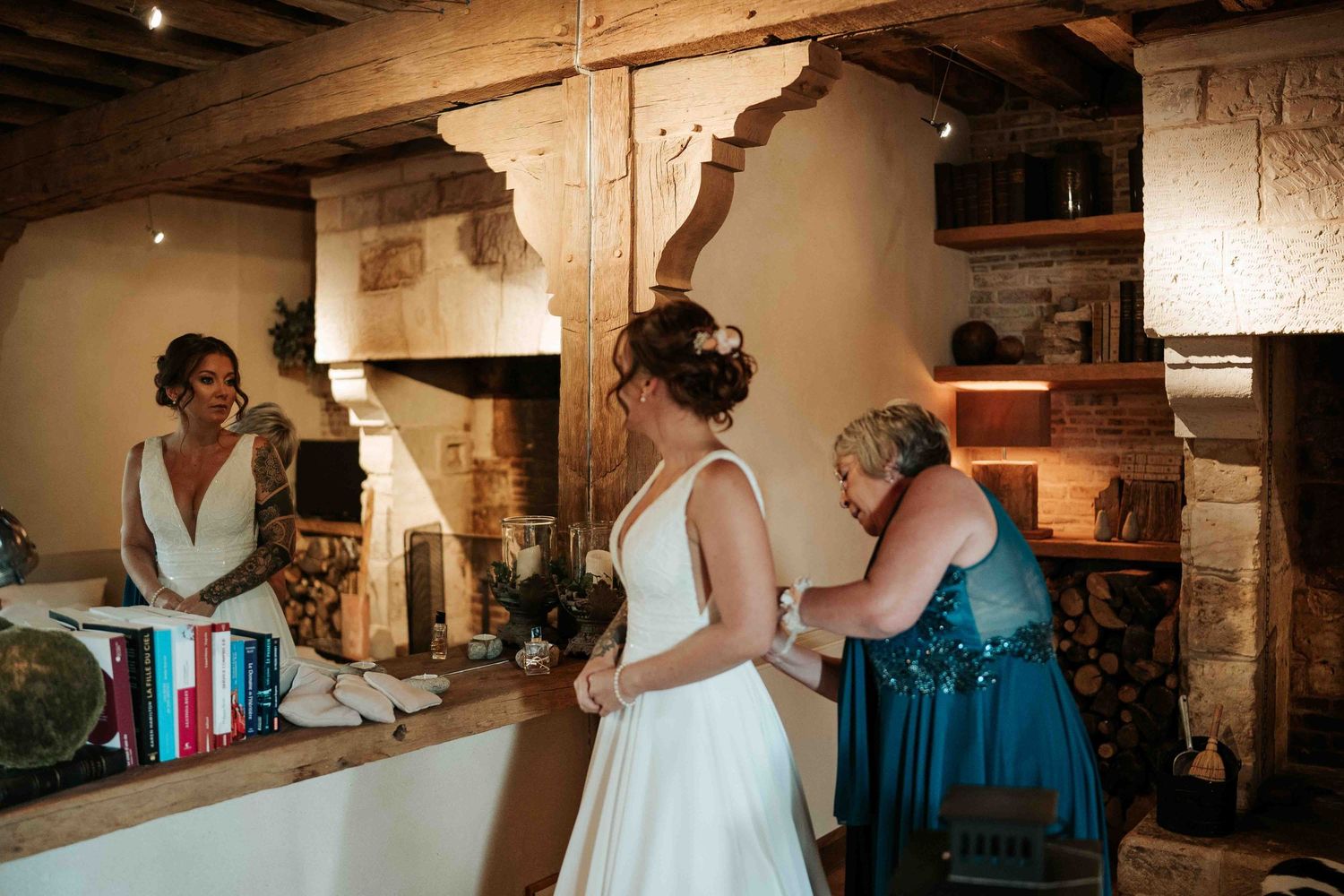 La mariée en robe blanche, assistée d'un invité, se trouve près d'une cheminée rustique en pierre pendant les préparatifs de mariage.