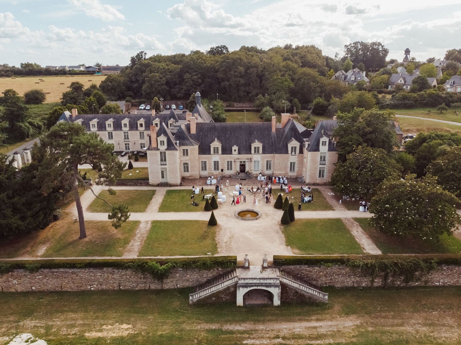 Vue aérienne d’un château lors d’un mariage – Mariés et invités rassemblés devant la façade principale et les jardins à la française.