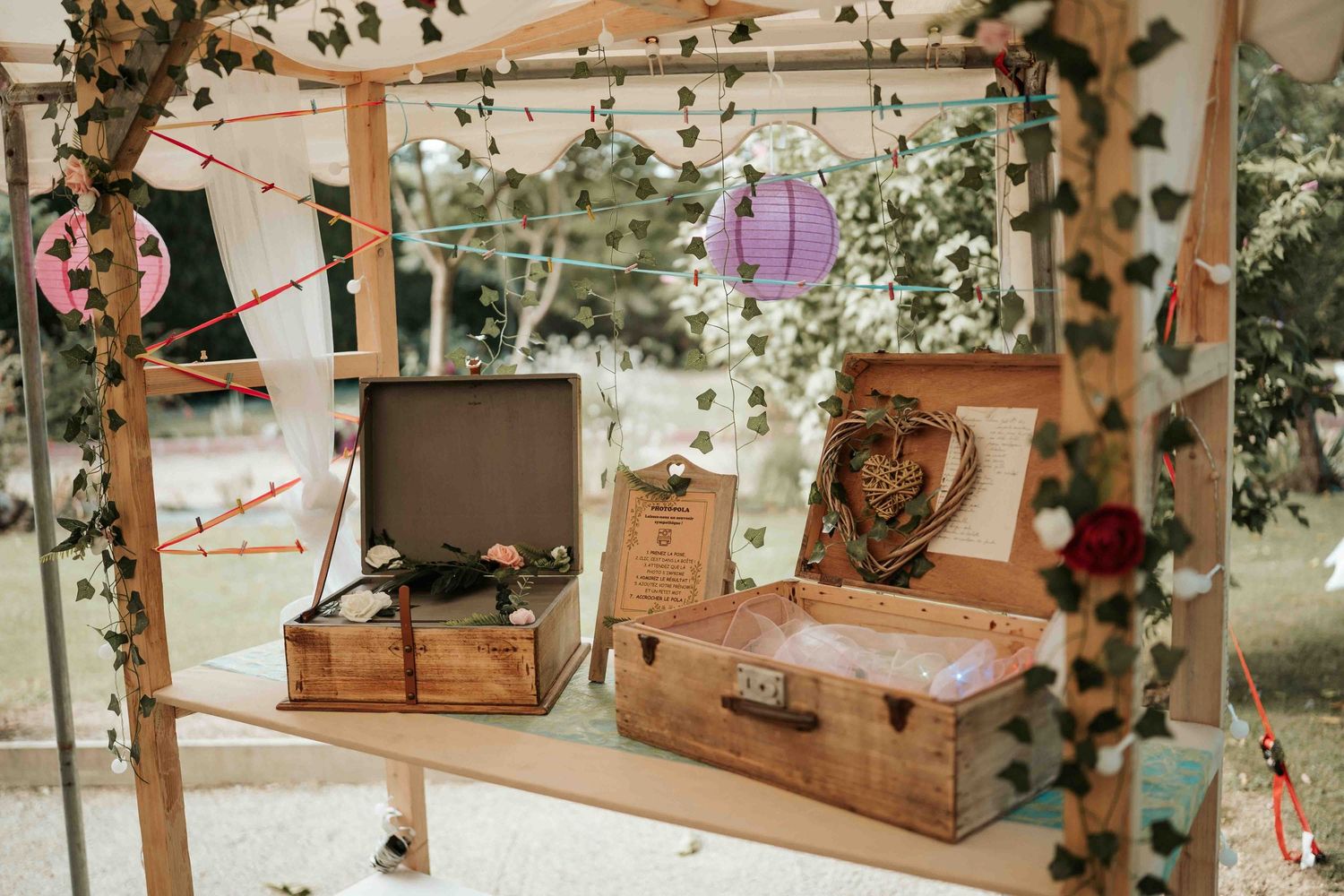 Valises vintage rustiques en bois décorées de lierre et de guirlandes, dans un lieu de réception de mariage en plein air.
