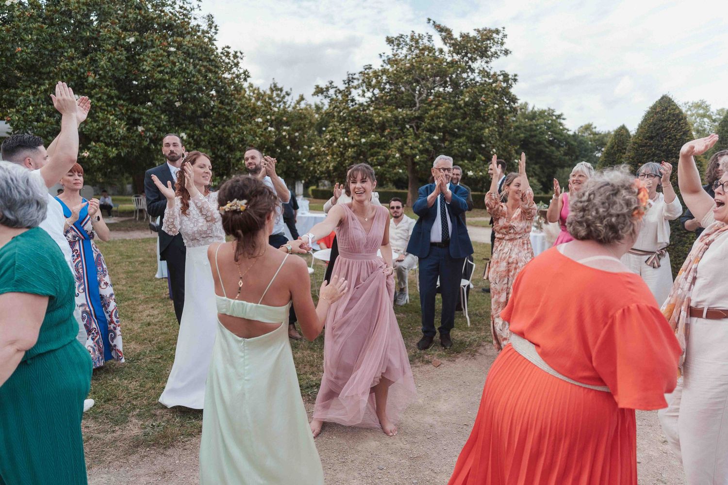 Réception de mariage colorée avec bal en plein air où les invités, vêtus de tenues éclatantes, dansent en cercle.