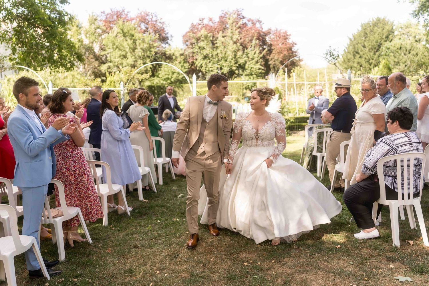 Les mariés descendent l'allée extérieure, entourés des applaudissements des invités, lors d'une cérémonie de mariage ensoleillée.