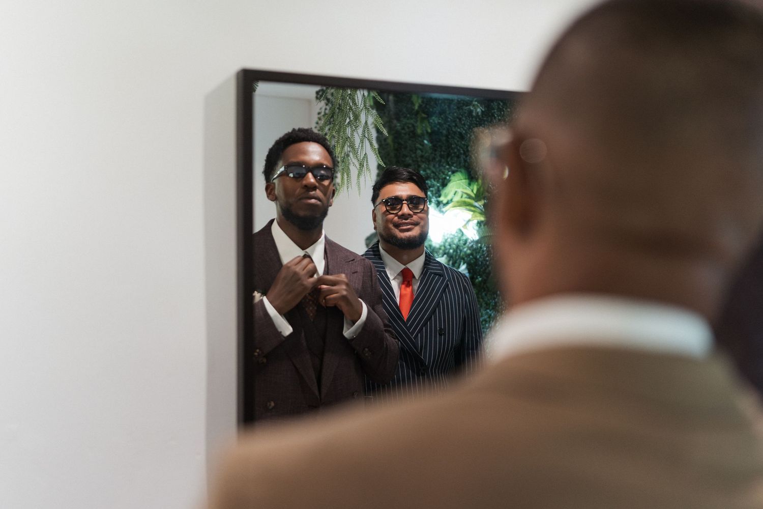 Deux hommes élégants en costume ajustent leur cravate en regardant leur reflet dans un miroir.