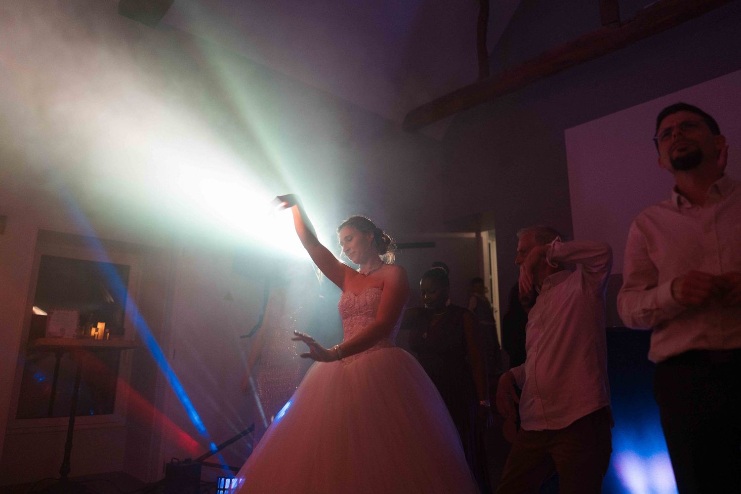 La mariée en robe de bal blanche danse, téléphone à la main, sous un éclairage de scène spectaculaire lors de la réception de mariage.