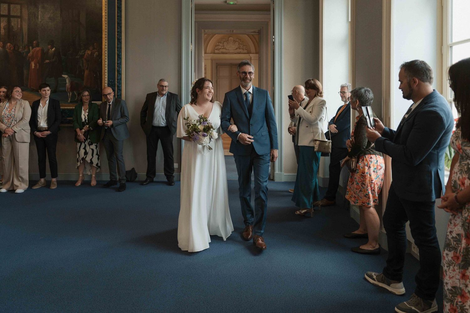 Les mariés descendent l'allée lors d'une élégante cérémonie de mariage en intérieur, sous les applaudissements des invités.