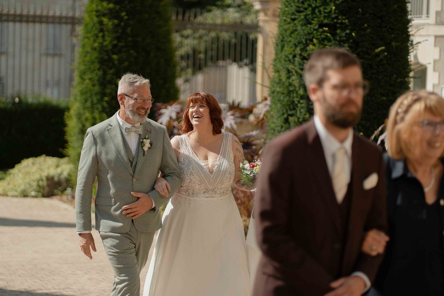 Les mariés, bras dessus bras dessous avec leurs invités, se promènent dans un jardin ensoleillé.
