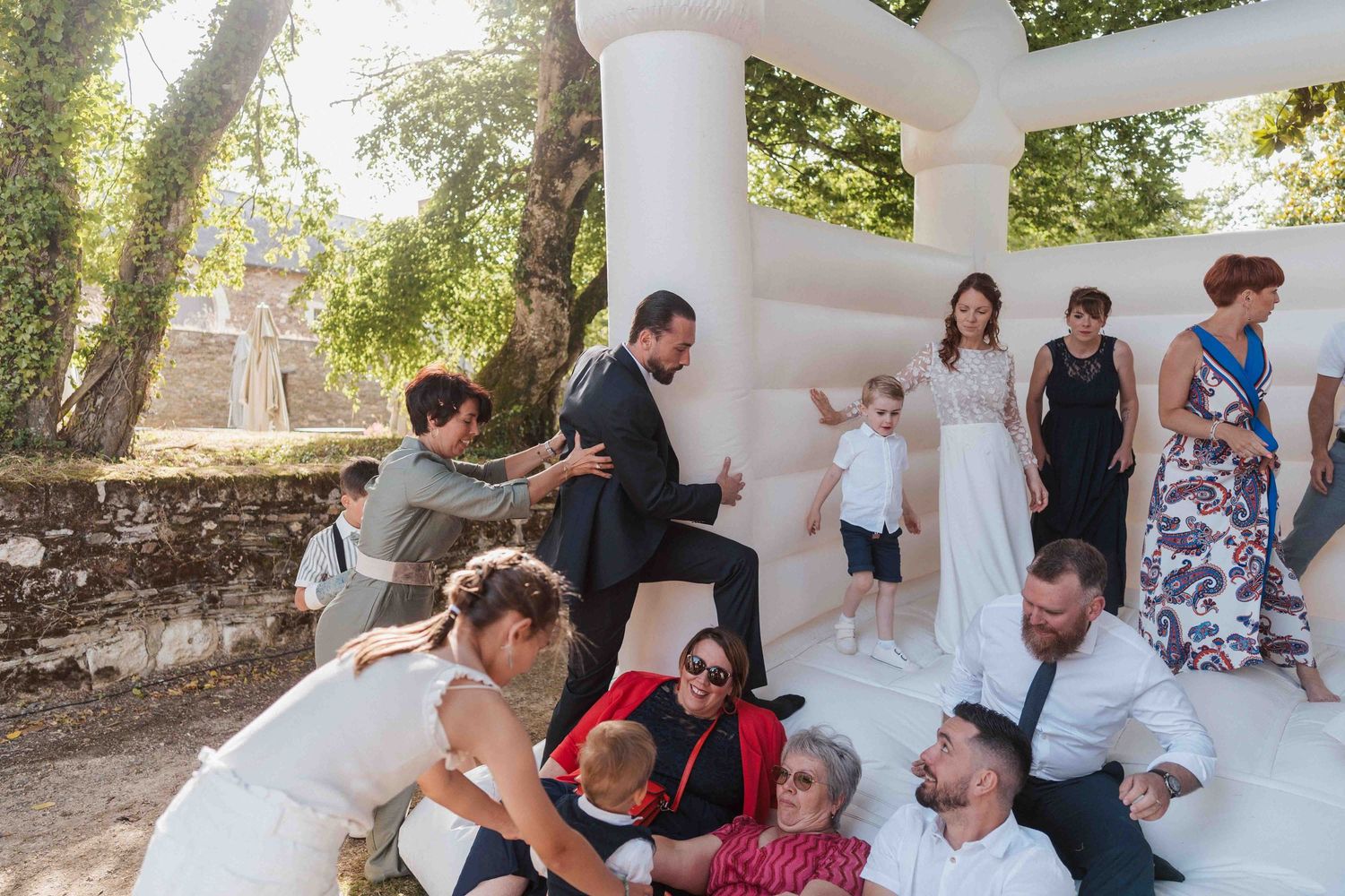 Les invités d'un mariage profitent d'un château gonflable blanc en extérieur, la mariée en robe blanche se joignant à la fête.