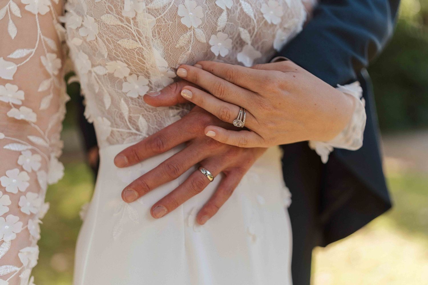 Gros plan sur les mains des jeunes mariés montrant leurs alliances sur la robe de dentelle de la mariée.