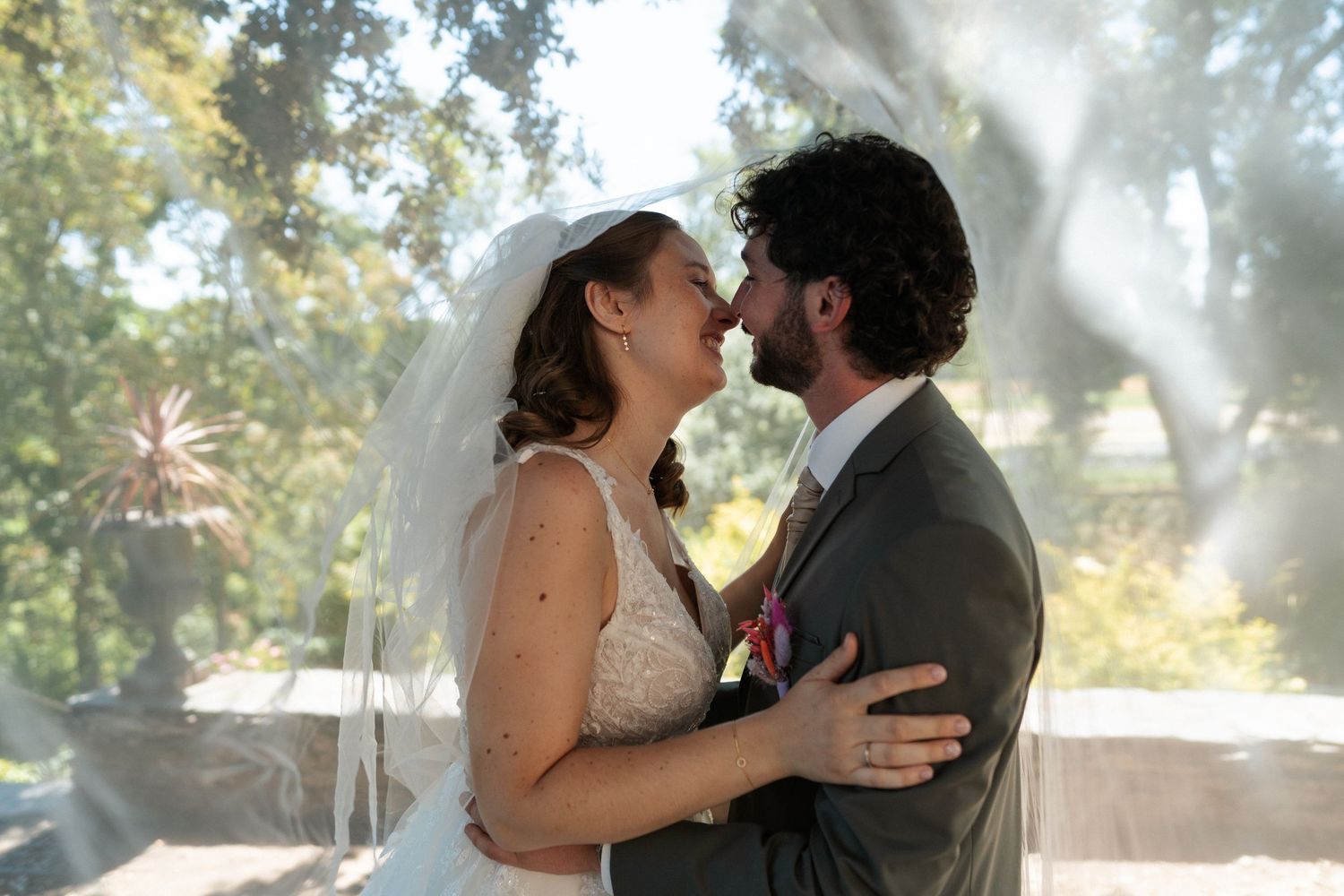 Bride and groom share a romantic kiss at outdoor wedding ceremony, bride wearing veil and lace dress.
