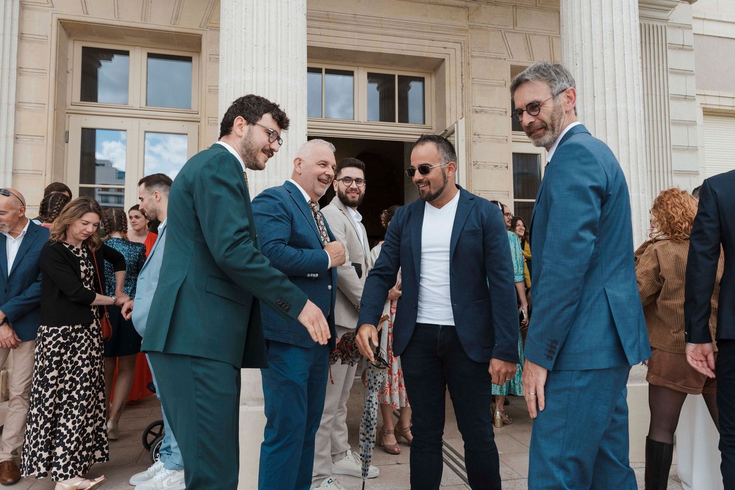 Accueil des invités devant la mairie lors d’un mariage – Marié en costume vert saluant ses proches dans une ambiance festive.