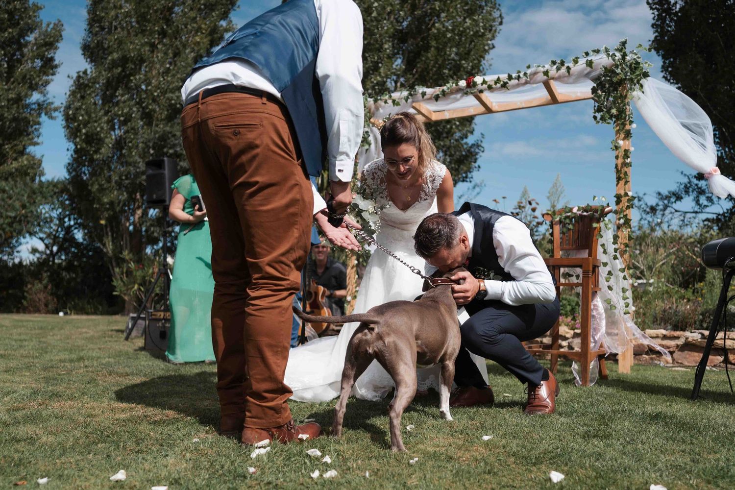 Les mariés caressent leur chien marron lors de la cérémonie de mariage en plein air sous une arche fleurie.