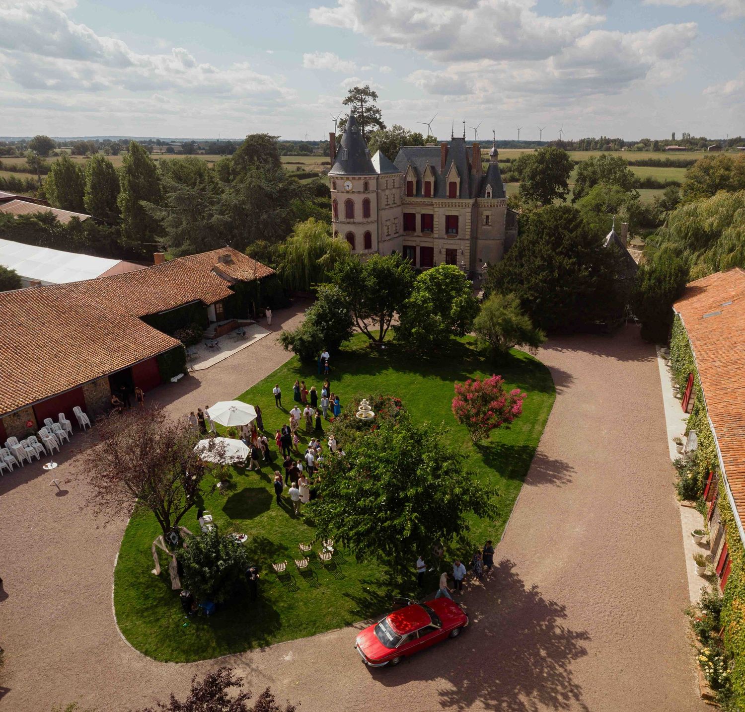 Vue aérienne d'un magnifique château français, lieu de mariage avec jardins soignés et voiture classique rouge.