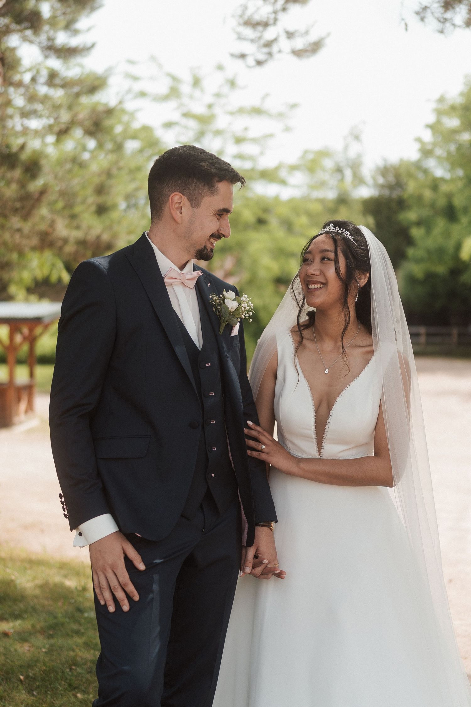 La mariée, vêtue d'un voile blanc, et le marié, en costume bleu marine, partagent un joyeux moment en plein air.