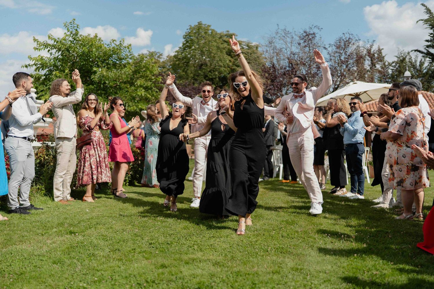 Les invités d'un mariage dansent et célèbrent joyeusement sur une pelouse verte sous un soleil radieux.