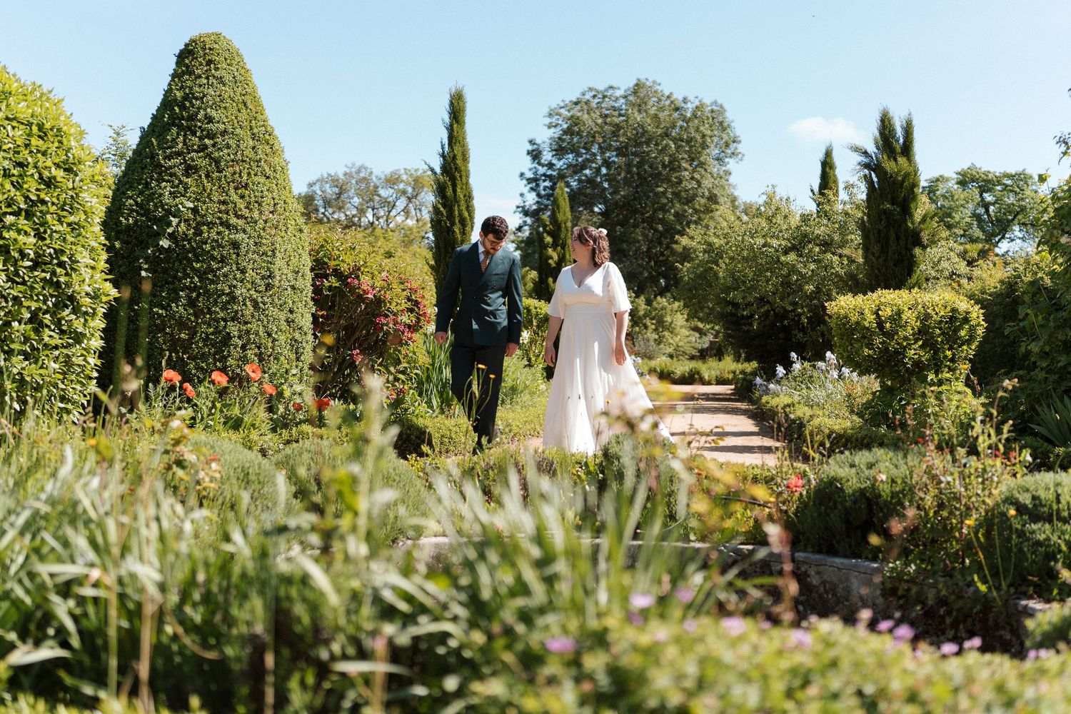 Mariés se promenant dans les jardins de l’Orangerie des Briottières aux Hauts-d’Anjou – Portrait naturel dans un cadre verdoyant et fleuri.